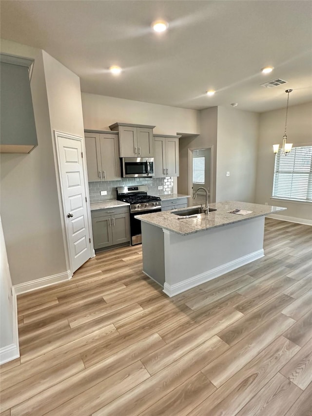 kitchen with visible vents, decorative backsplash, gray cabinets, stainless steel appliances, and a sink