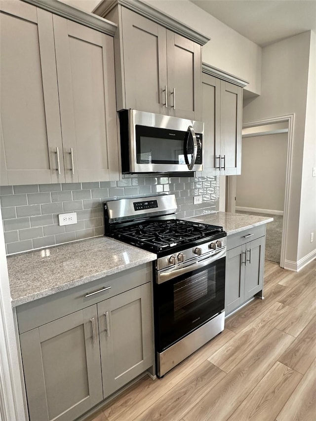 kitchen with light wood finished floors, decorative backsplash, appliances with stainless steel finishes, light stone counters, and gray cabinetry