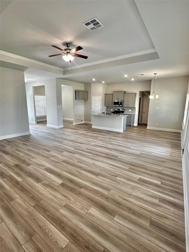 unfurnished living room with light wood finished floors, visible vents, a raised ceiling, and a ceiling fan