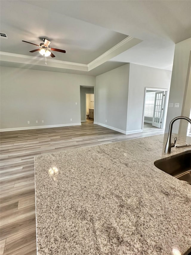 unfurnished living room featuring a ceiling fan, a raised ceiling, a sink, and baseboards