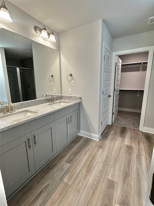 full bath with a walk in closet, a sink, a shower stall, and wood finished floors