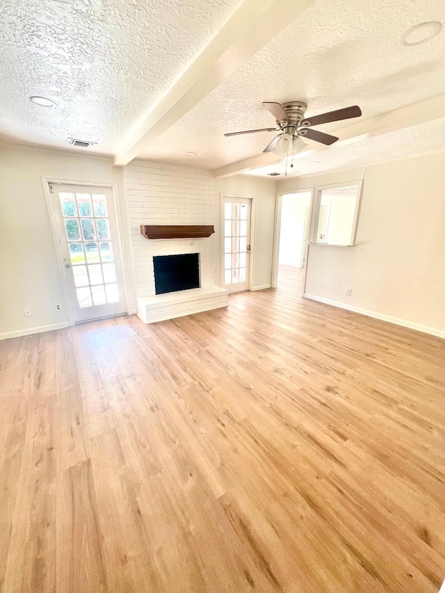 unfurnished living room featuring ceiling fan, a brick fireplace, a textured ceiling, and light hardwood / wood-style flooring