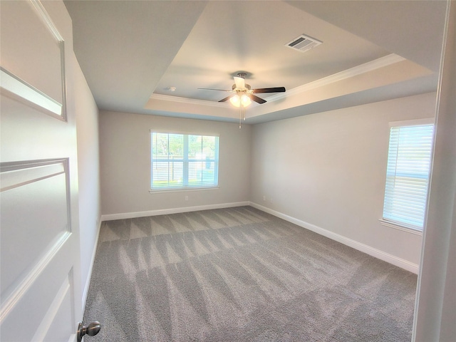 carpeted spare room with a raised ceiling, ornamental molding, and ceiling fan