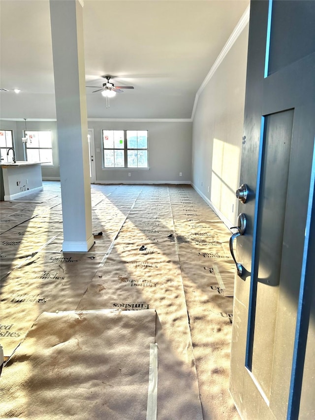 living area featuring a wealth of natural light, crown molding, baseboards, and ceiling fan