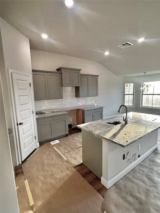 kitchen featuring tasteful backsplash, light stone countertops, vaulted ceiling, gray cabinets, and a sink