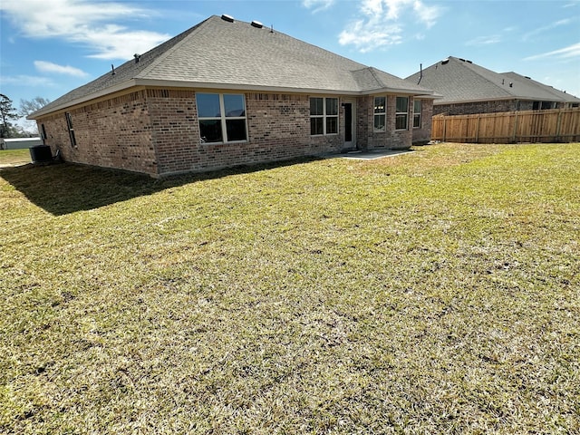 back of property featuring brick siding, fence, roof with shingles, a lawn, and a patio area