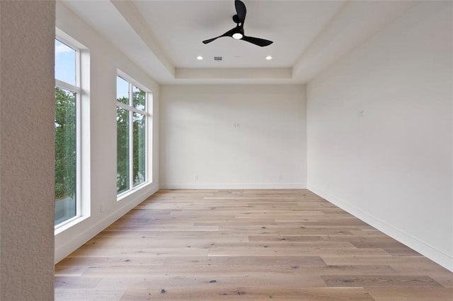 spare room with ceiling fan, a raised ceiling, and light hardwood / wood-style flooring