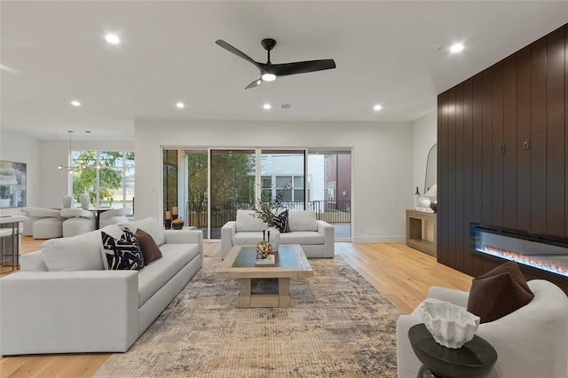 living room with a fireplace, light hardwood / wood-style floors, ceiling fan, and wood walls