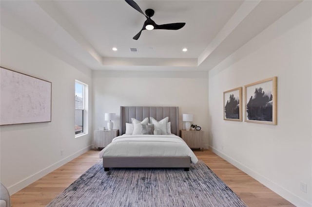 bedroom featuring ceiling fan, a tray ceiling, and light hardwood / wood-style floors