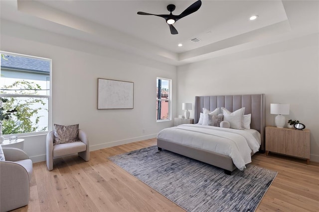 bedroom with radiator heating unit, light hardwood / wood-style flooring, a raised ceiling, and ceiling fan