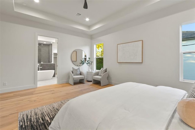 bedroom with hardwood / wood-style flooring, ensuite bath, a tray ceiling, and multiple windows