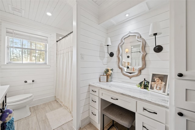 bathroom featuring vanity, toilet, walk in shower, and wood walls