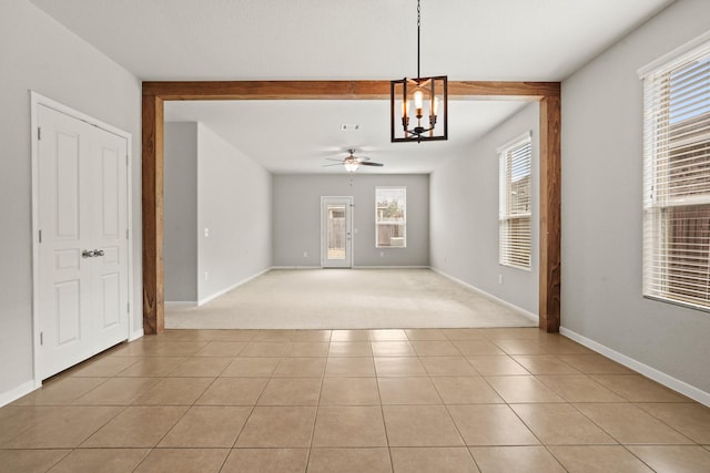 interior space featuring ceiling fan with notable chandelier, beamed ceiling, light tile patterned floors, and a wealth of natural light