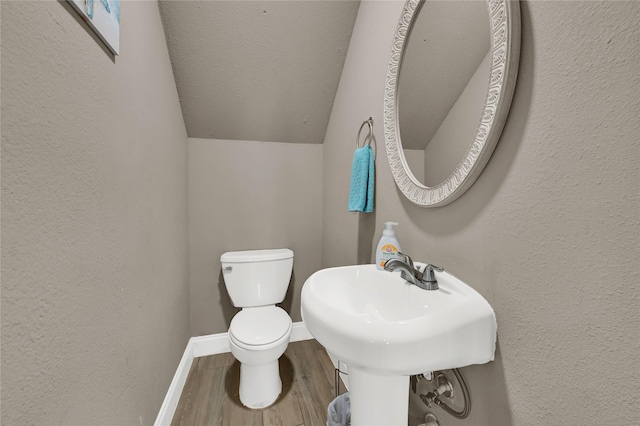 bathroom with hardwood / wood-style floors, lofted ceiling, sink, toilet, and a textured ceiling