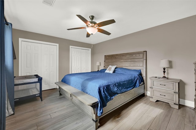 bedroom with light wood finished floors, two closets, visible vents, a ceiling fan, and baseboards