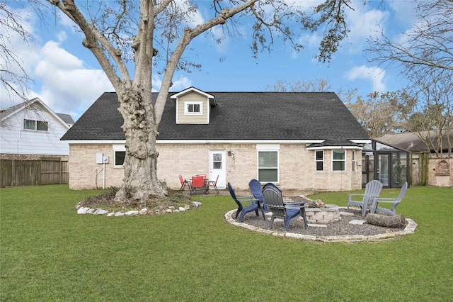 rear view of property with an outdoor fire pit, roof with shingles, a lawn, and brick siding