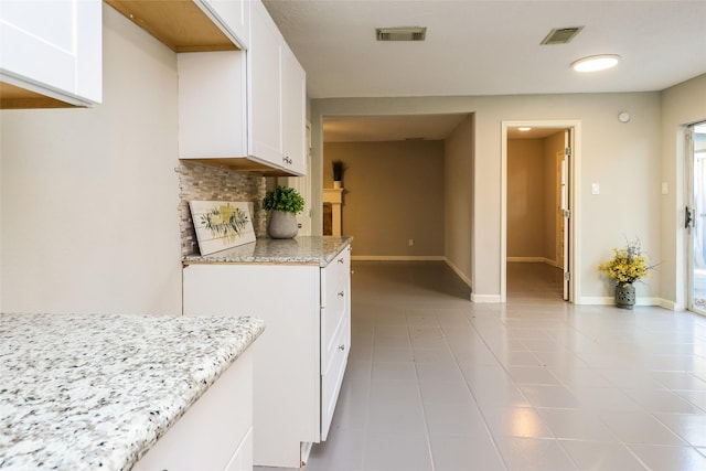 kitchen with white cabinetry, light stone countertops, light tile patterned flooring, and tasteful backsplash