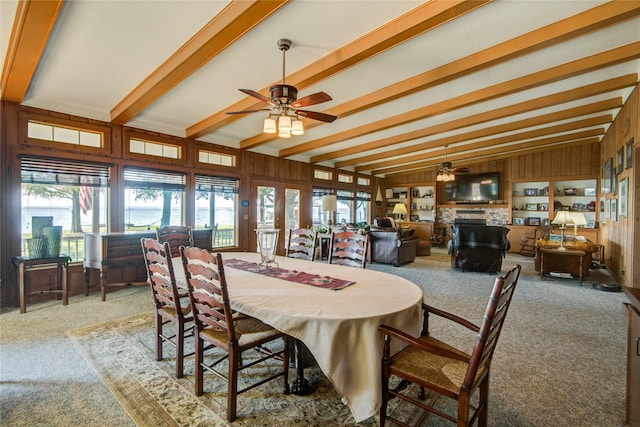 carpeted dining room featuring wooden walls, a wealth of natural light, ceiling fan, and lofted ceiling with beams