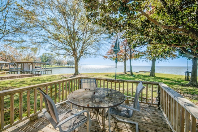 wooden terrace with outdoor dining space, a water view, and a yard