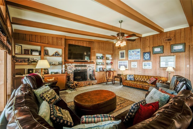 living area featuring wood walls, ceiling fan, a fireplace, beam ceiling, and visible vents