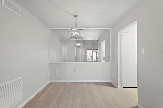 unfurnished dining area with a notable chandelier and light wood-type flooring