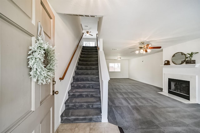 stairs featuring a fireplace with flush hearth, visible vents, a ceiling fan, tile patterned floors, and carpet