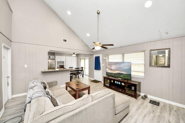 living room with ceiling fan, high vaulted ceiling, and light wood-type flooring