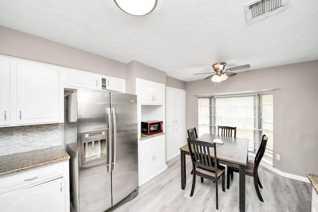 kitchen featuring white cabinetry, dark stone countertops, light hardwood / wood-style floors, and stainless steel fridge with ice dispenser