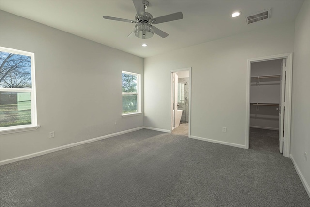 unfurnished bedroom featuring ensuite bathroom, dark colored carpet, a spacious closet, ceiling fan, and a closet