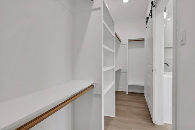 walk in closet with light hardwood / wood-style floors and a barn door