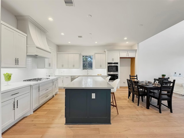 kitchen with light hardwood / wood-style flooring, white cabinetry, backsplash, stainless steel appliances, and a center island