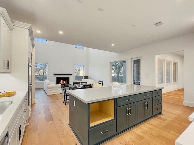 kitchen featuring white cabinetry, stainless steel dishwasher, a kitchen island, and light wood-type flooring