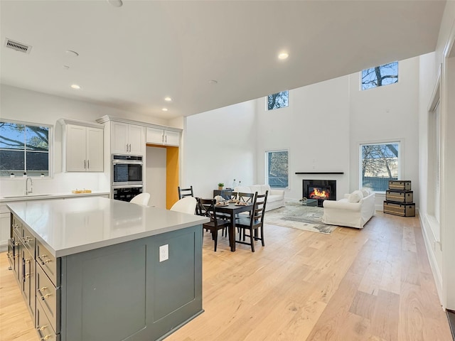 kitchen with gray cabinets, sink, a center island, stainless steel double oven, and light wood-type flooring