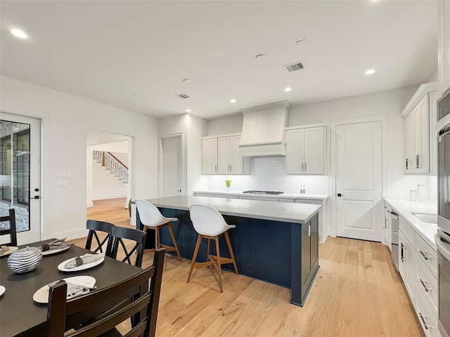 kitchen with a kitchen breakfast bar, a center island, custom exhaust hood, and white cabinets