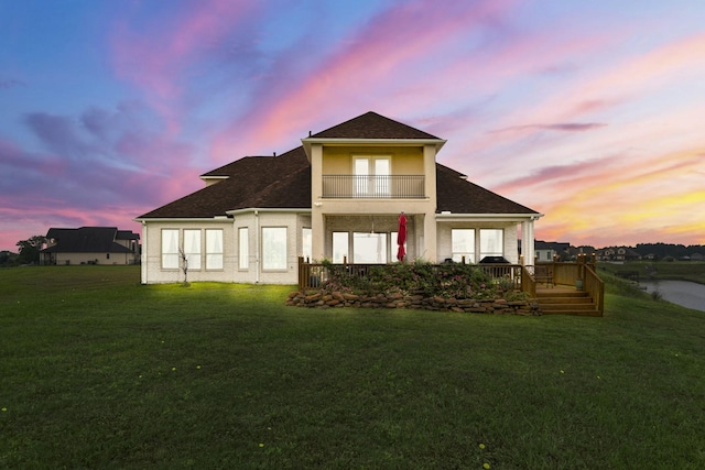 back house at dusk featuring a lawn and a balcony