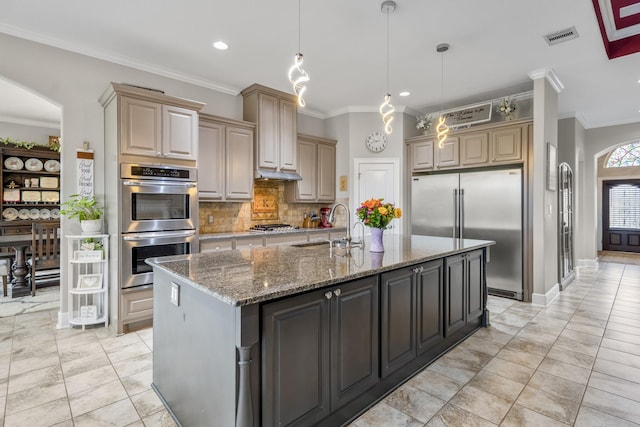 kitchen with sink, hanging light fixtures, appliances with stainless steel finishes, an island with sink, and decorative backsplash