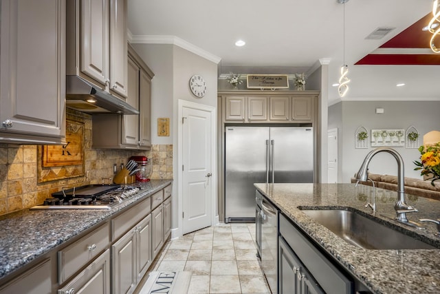 kitchen with decorative light fixtures, sink, dark stone counters, ornamental molding, and stainless steel appliances