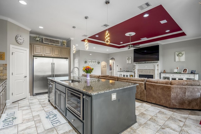 kitchen with sink, gray cabinetry, dark stone countertops, a tray ceiling, and a kitchen island with sink