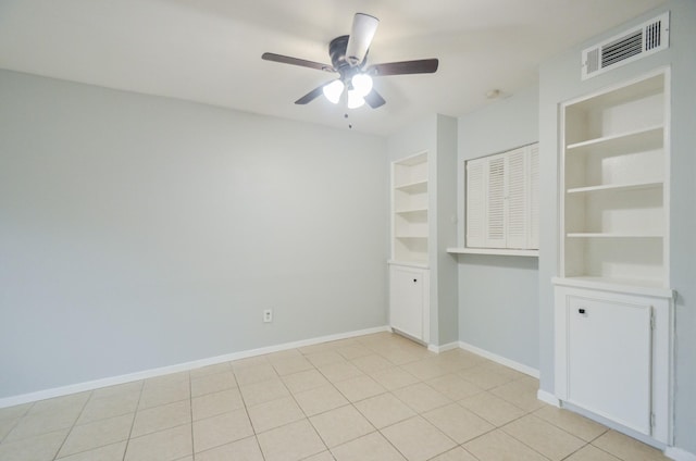 tiled empty room with ceiling fan and built in shelves