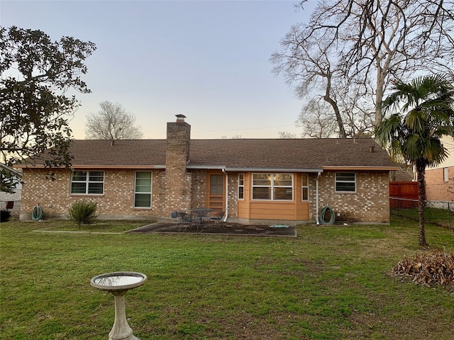 view of front of property featuring fence, roof with shingles, a chimney, a front lawn, and brick siding