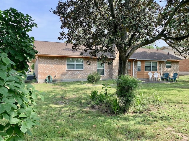 back of property with brick siding, a lawn, and roof with shingles