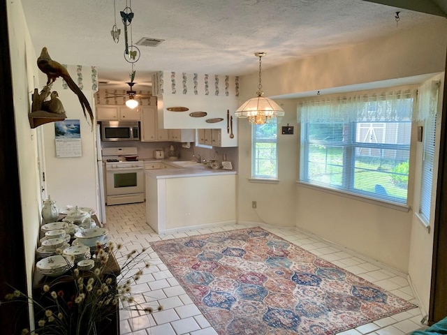 kitchen featuring white range with gas cooktop, stainless steel microwave, light countertops, a textured ceiling, and light tile patterned flooring