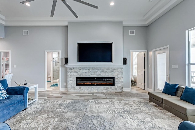 living room featuring ceiling fan, a high ceiling, a tile fireplace, and light hardwood / wood-style flooring