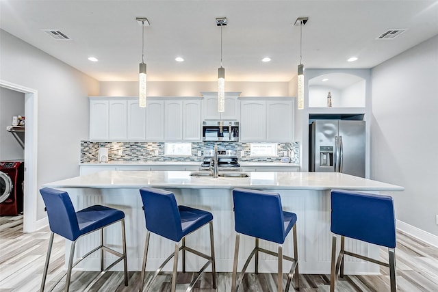 kitchen featuring sink, backsplash, stainless steel appliances, white cabinets, and a center island with sink