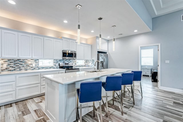 kitchen featuring appliances with stainless steel finishes, white cabinetry, sink, hanging light fixtures, and a kitchen island with sink