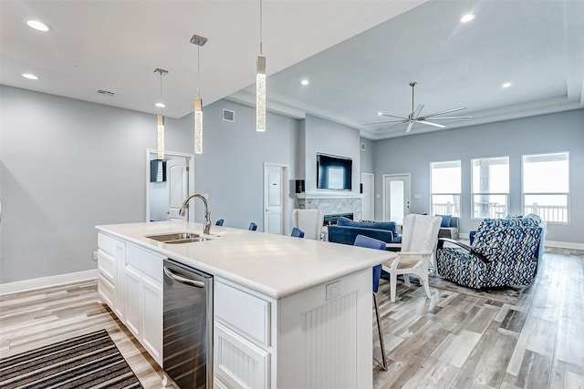 kitchen featuring decorative light fixtures, white cabinetry, sink, a kitchen island with sink, and light wood-type flooring