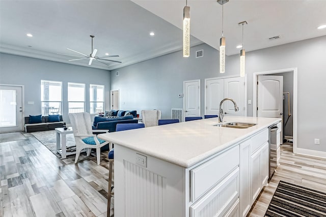 kitchen featuring white cabinetry, an island with sink, sink, hanging light fixtures, and light wood-type flooring