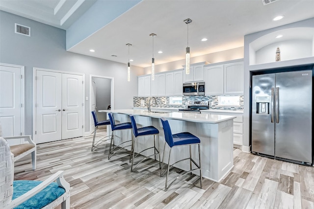 kitchen featuring appliances with stainless steel finishes, decorative light fixtures, an island with sink, sink, and white cabinets