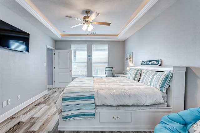 bedroom with light hardwood / wood-style flooring, ornamental molding, a raised ceiling, and ceiling fan