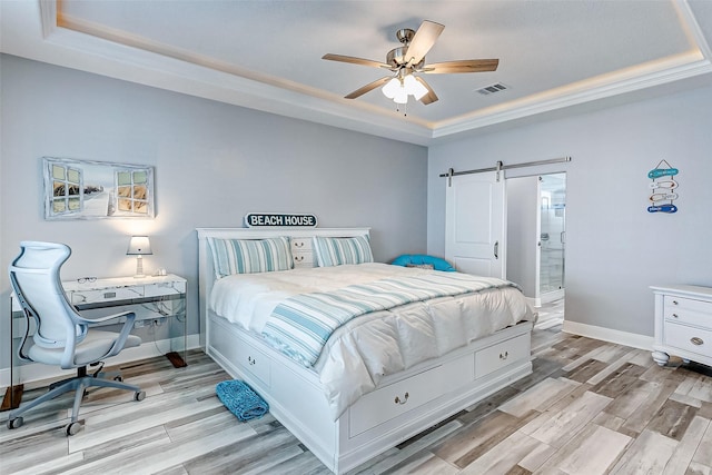 bedroom with a raised ceiling, ceiling fan, a barn door, and light hardwood / wood-style floors